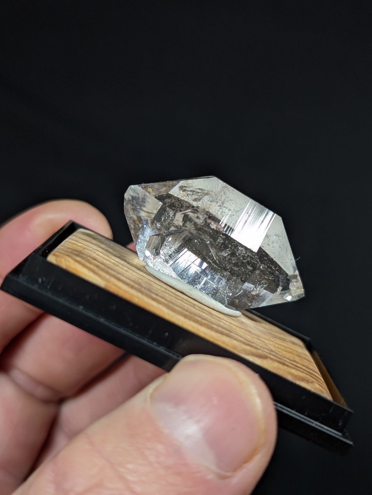 A clear, faceted quartz crystal with dark inclusions rests on a wooden display stand.