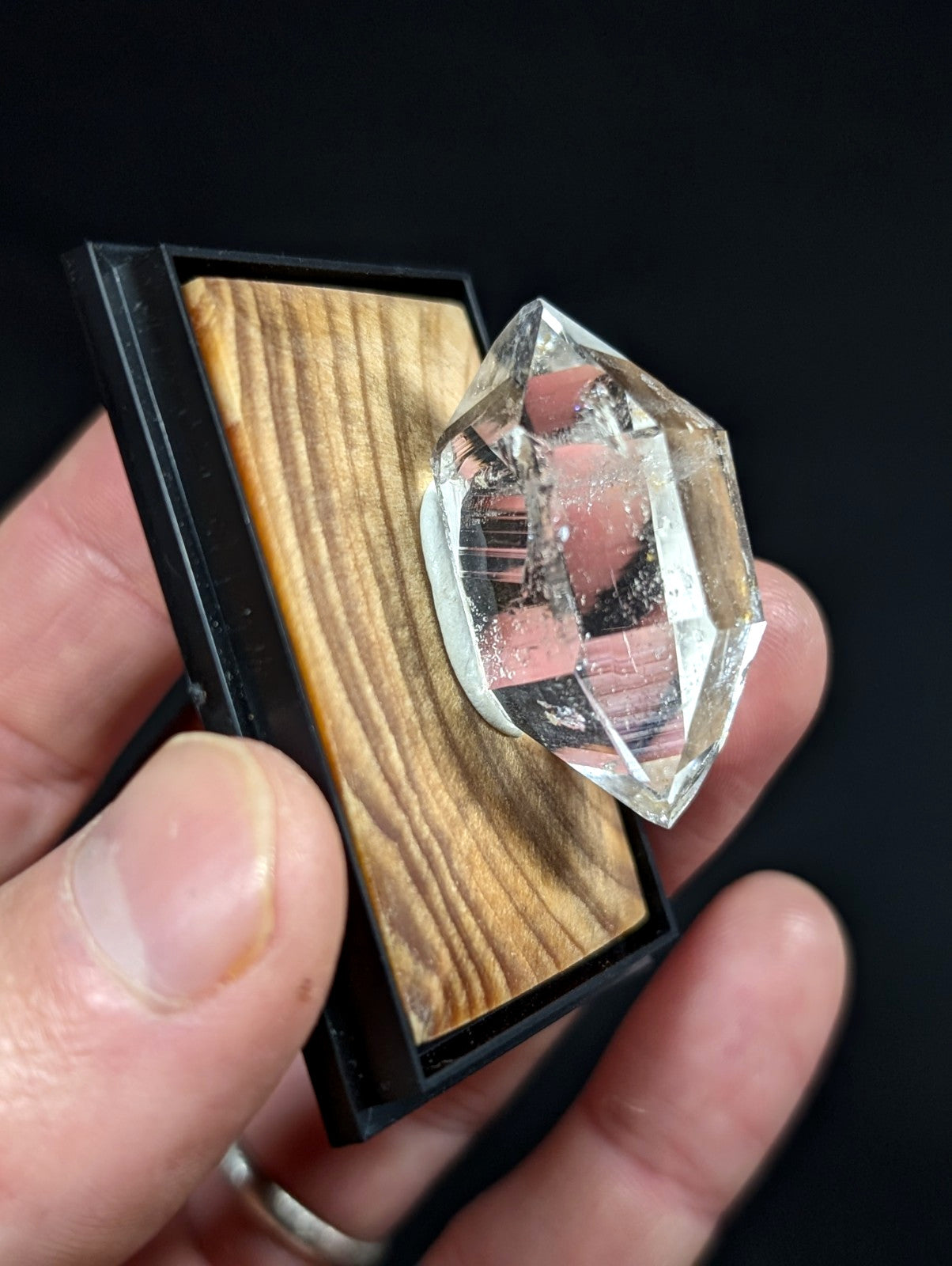 A clear, faceted quartz crystal mounted on a wooden base within a black display case.