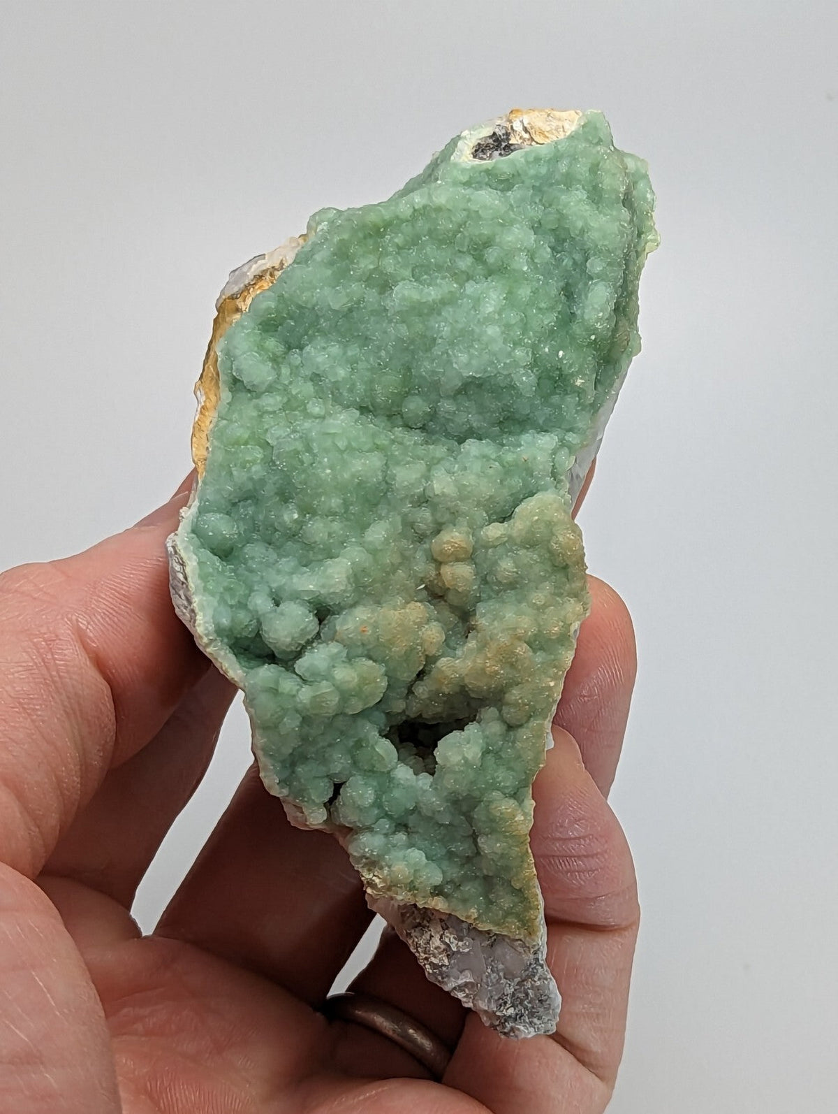 A hand holds a vibrant green, crystalline mineral specimen with a textured surface and subtle yellowish patches.