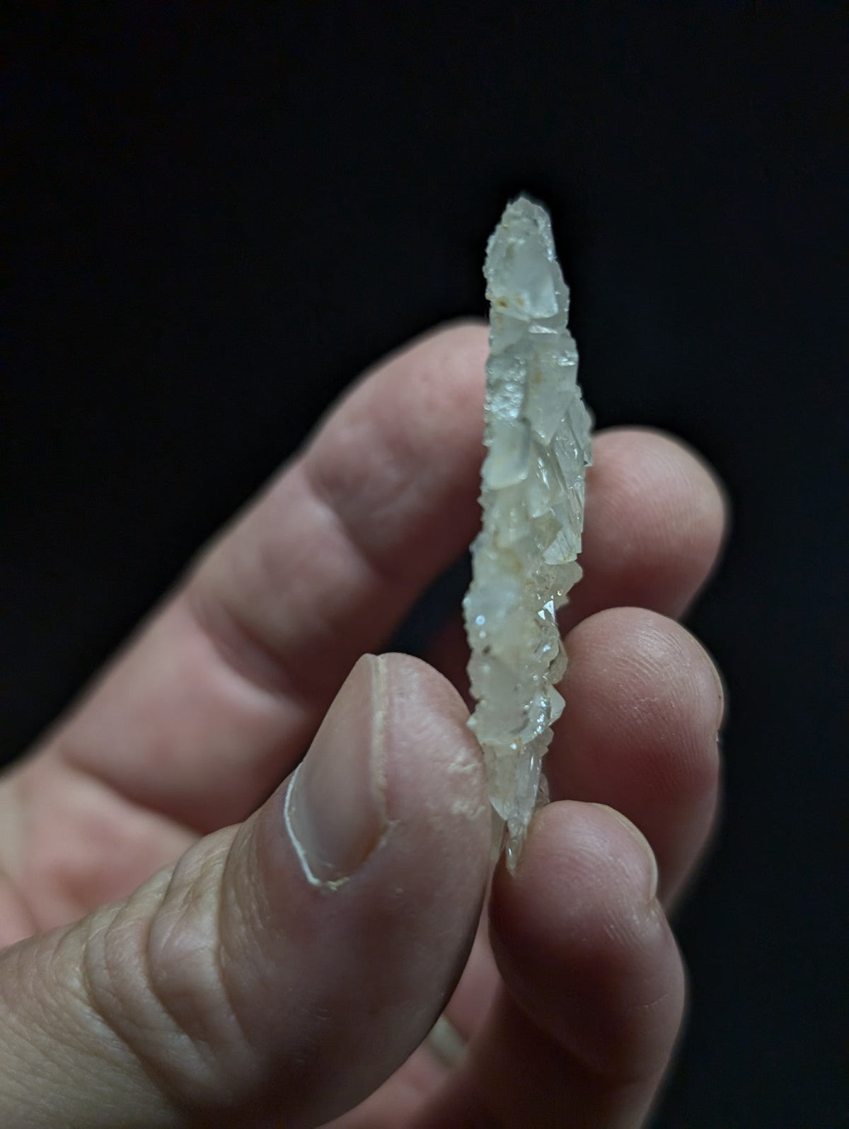 A translucent, pale green crystal with a jagged, faceted surface held between fingers.