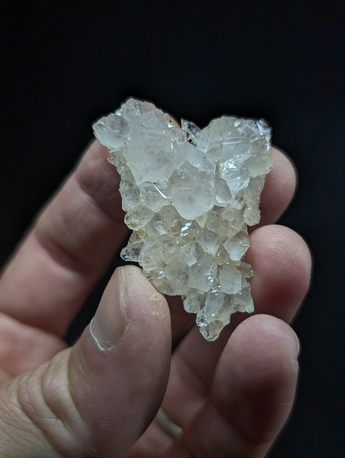 A translucent, crystalline mineral cluster with a jagged, faceted surface and pale, almost colorless hue.