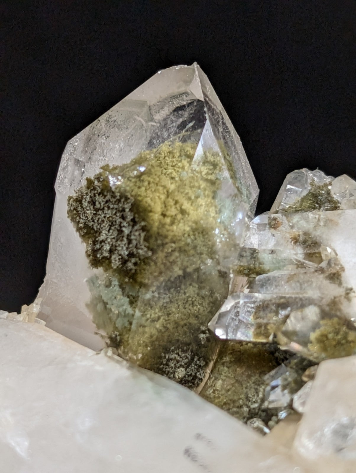 A clear quartz crystal cluster with greenish moss-like inclusions.