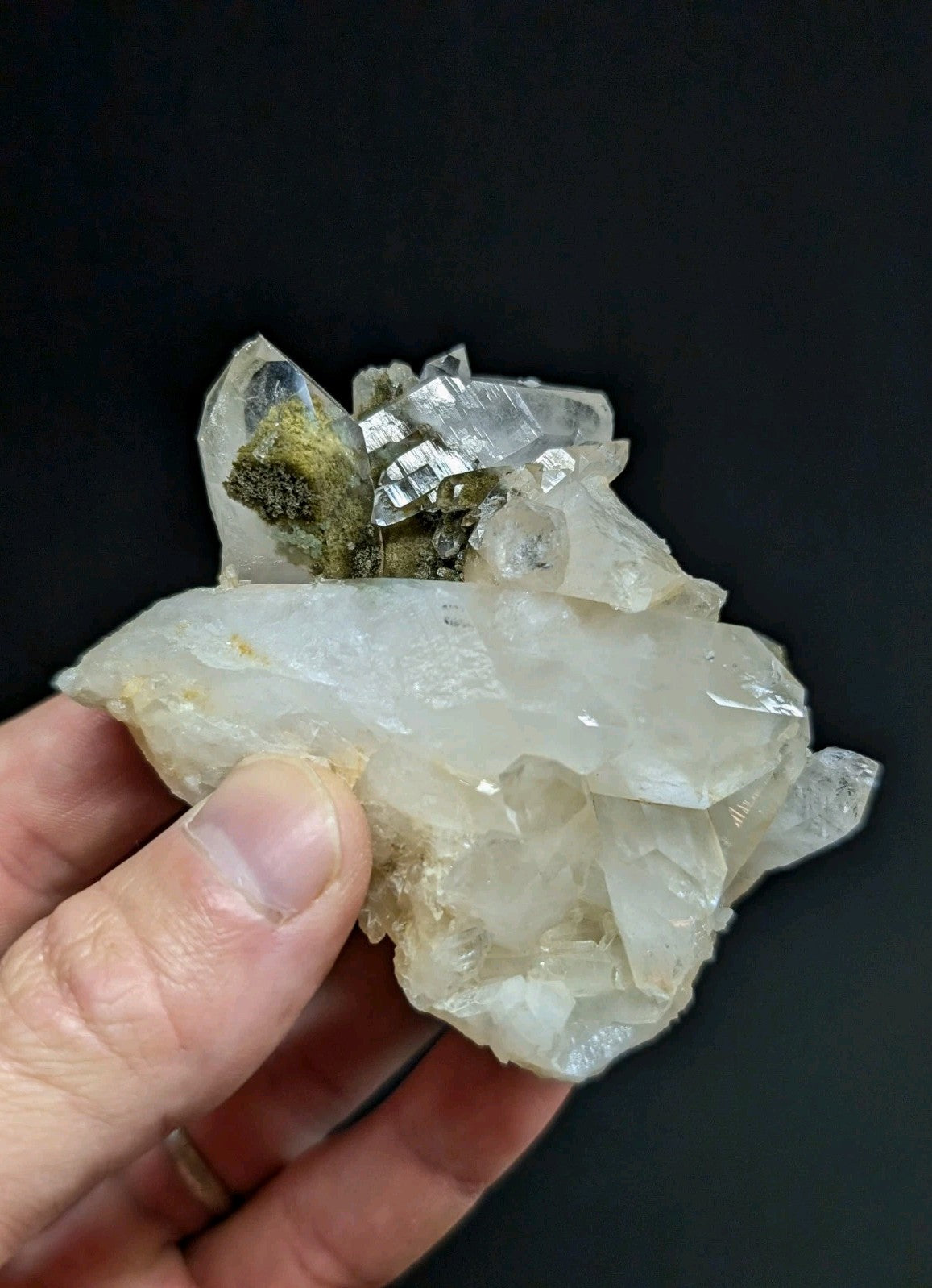 A translucent white quartz crystal cluster with sharp, faceted points and a small patch of greenish mineral growth.