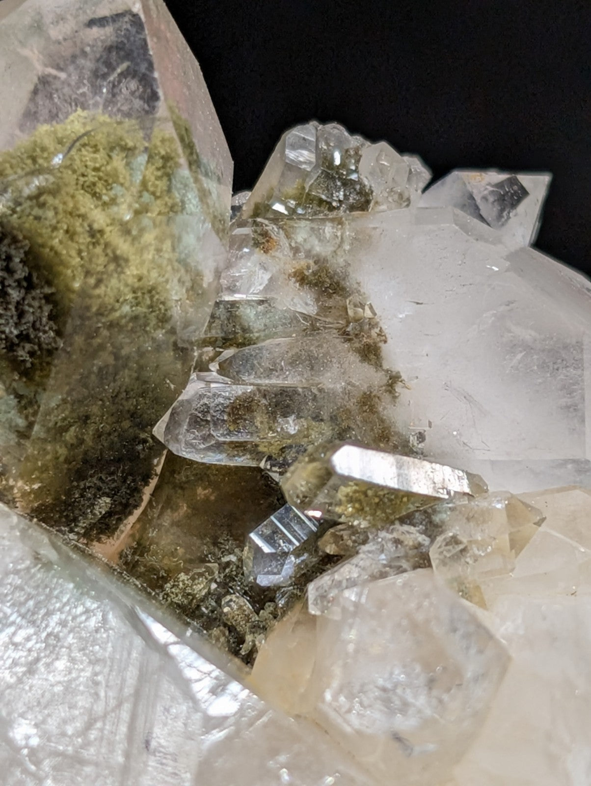 A translucent quartz crystal cluster with greenish-yellow moss-like inclusions and metallic silver mineral veins.