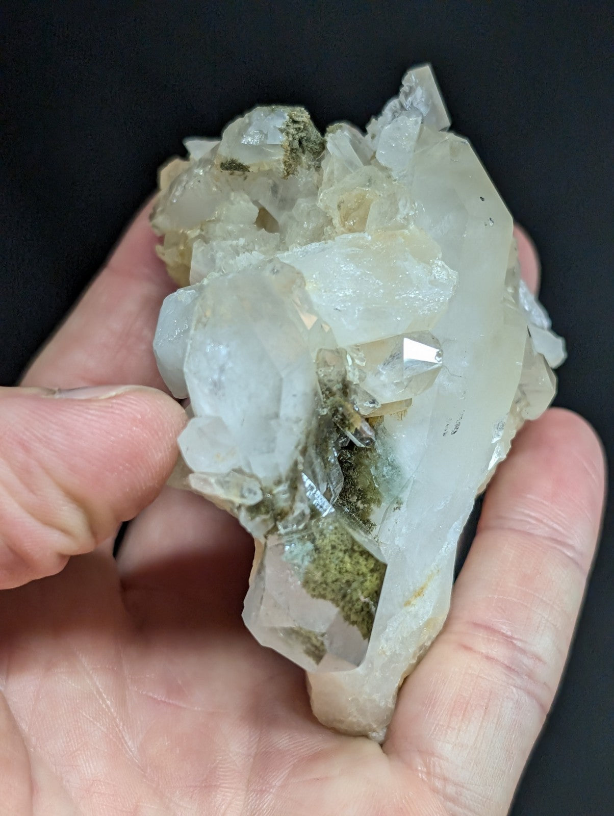 A translucent white quartz crystal cluster with greenish mineral inclusions, held gently in a hand.