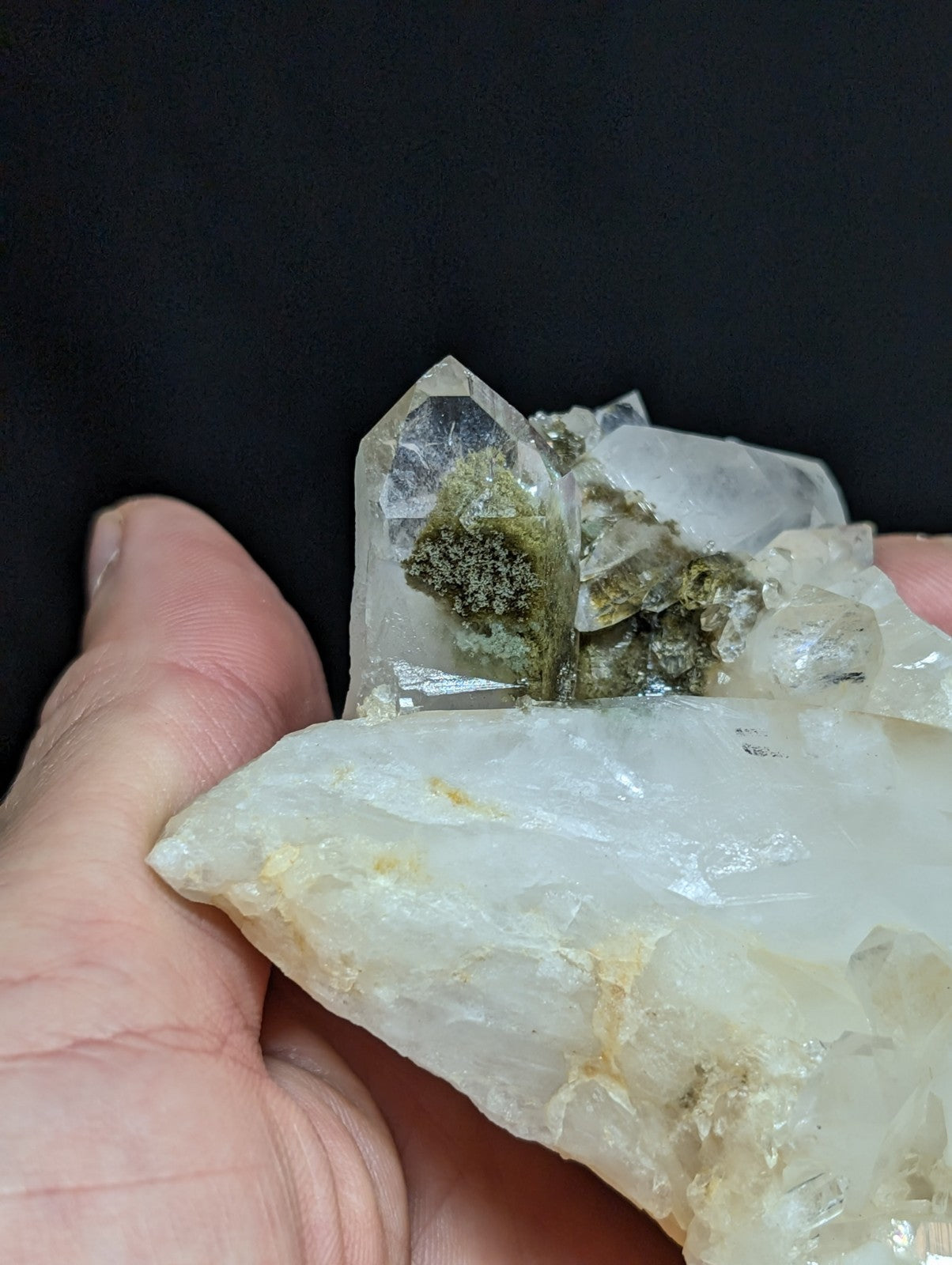 A translucent quartz crystal cluster with green moss-like growths nestled among its clear, faceted formations.