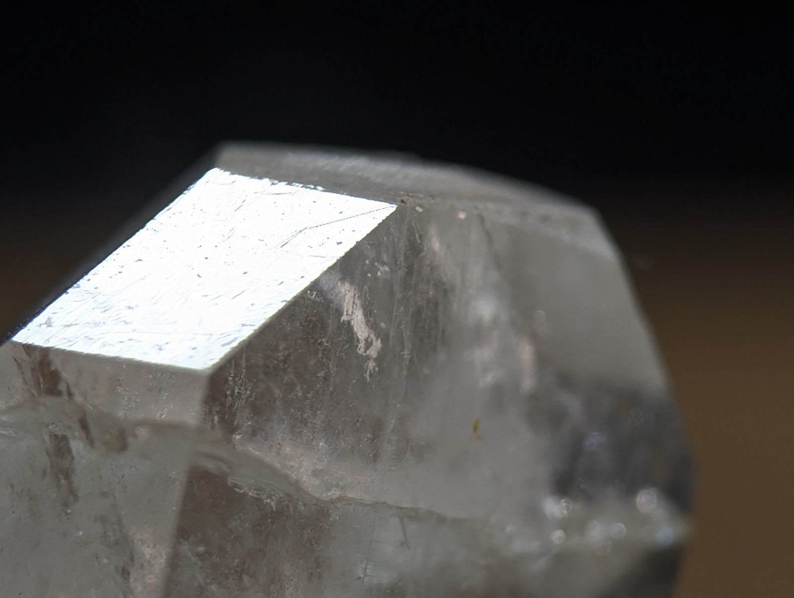 A translucent, clear quartz crystal with a prominent flat, reflective face and natural facets.