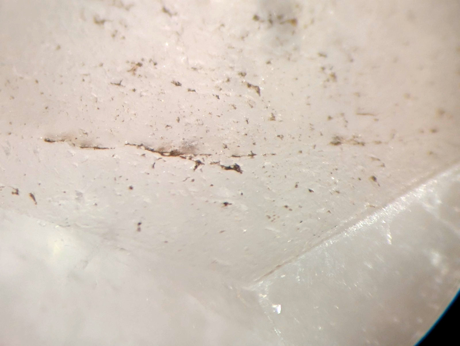 A white, slightly textured surface with scattered dark specks and a faint crack running across it.