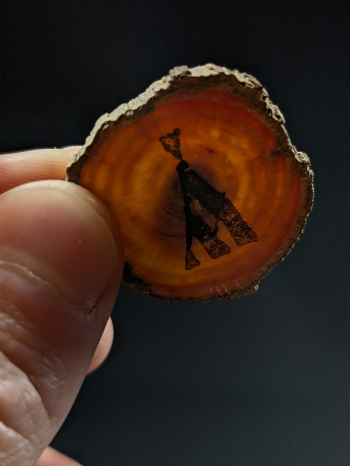 A hand holds a circular translucent orange agate slice with metal clock hands from a faden quartz cluster base