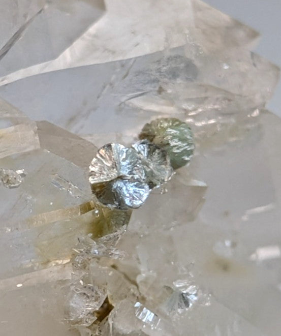 A cluster of metallic silvery leaf-shaped crystals atop translucent faden quartz with uv reactive blue-green cookeite from arkansas