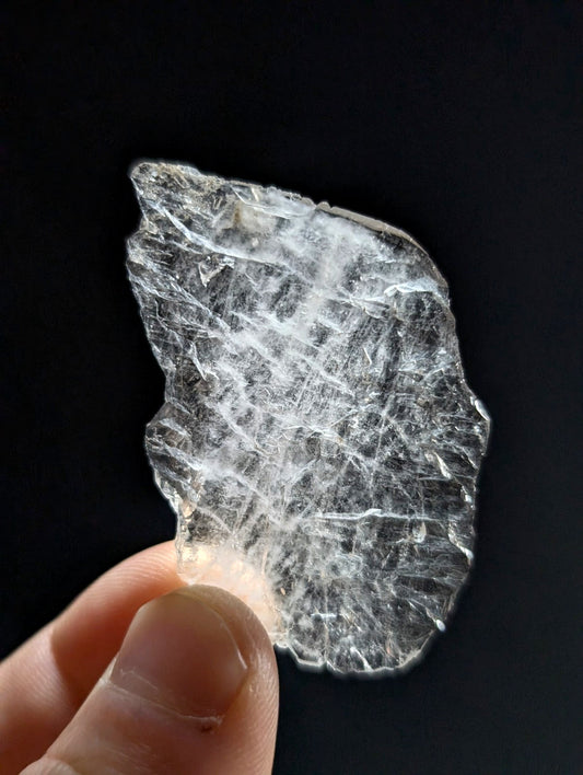 A translucent, clear crystal fragment with a delicate web-like internal pattern and jagged edges.