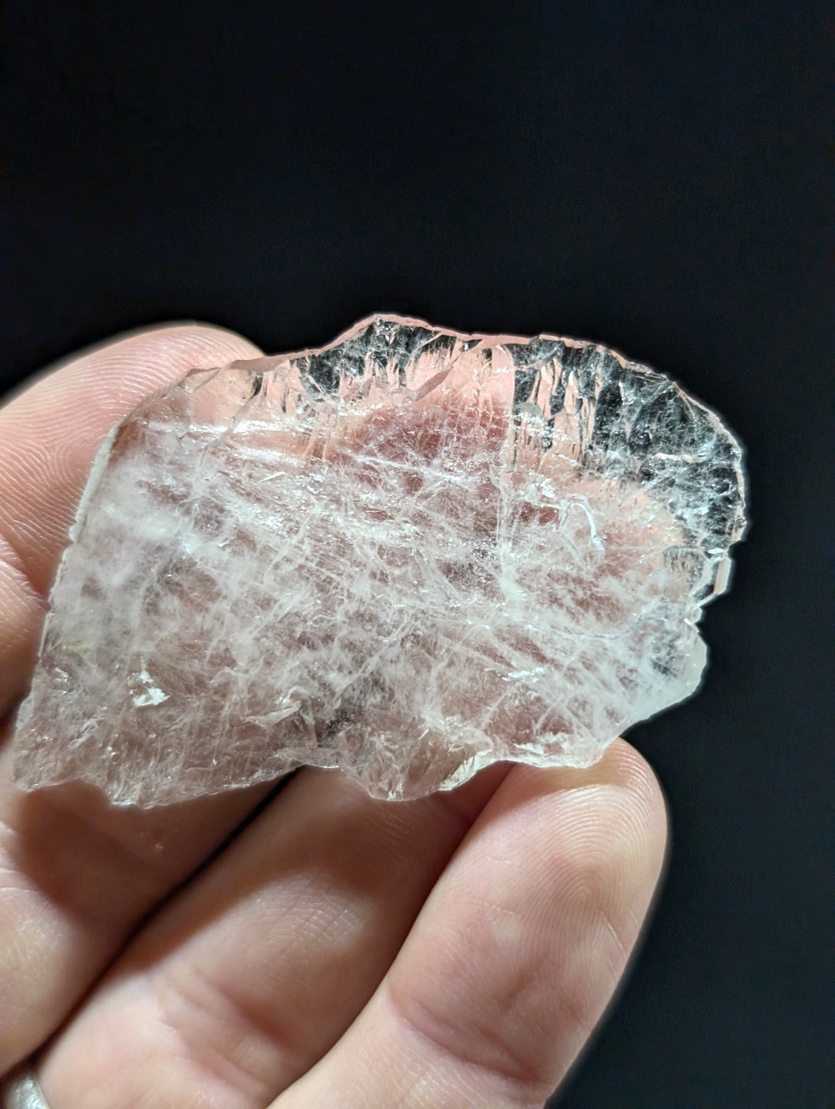 A translucent, pale pink crystal with a rough, jagged surface and visible internal striations.