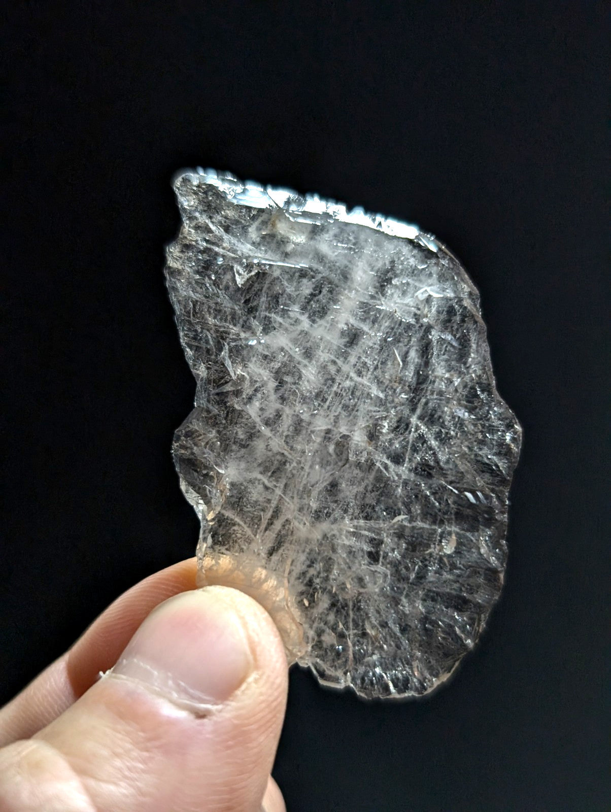 A translucent, clear quartz crystal with a rough, jagged edge and visible internal fibrous inclusions.