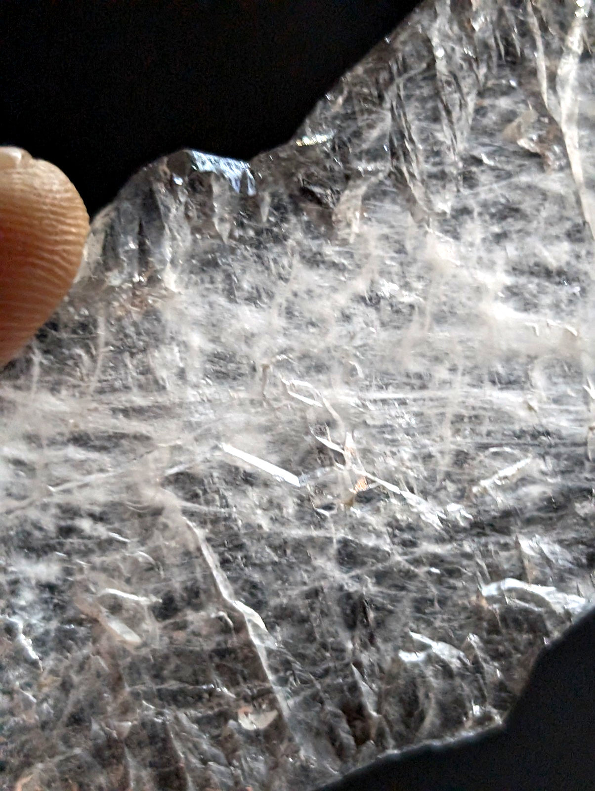 A translucent, clear quartz crystal with intricate white fibrous inclusions and a rough, jagged surface.