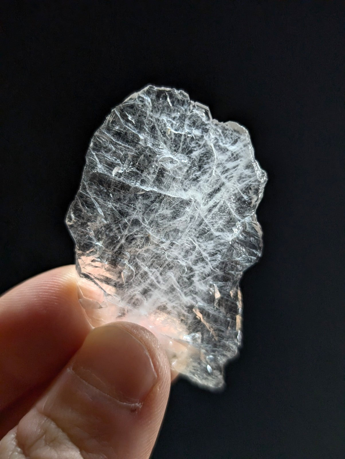 A translucent, clear quartz crystal with intricate internal fiber-like patterns and a rough, natural edge.