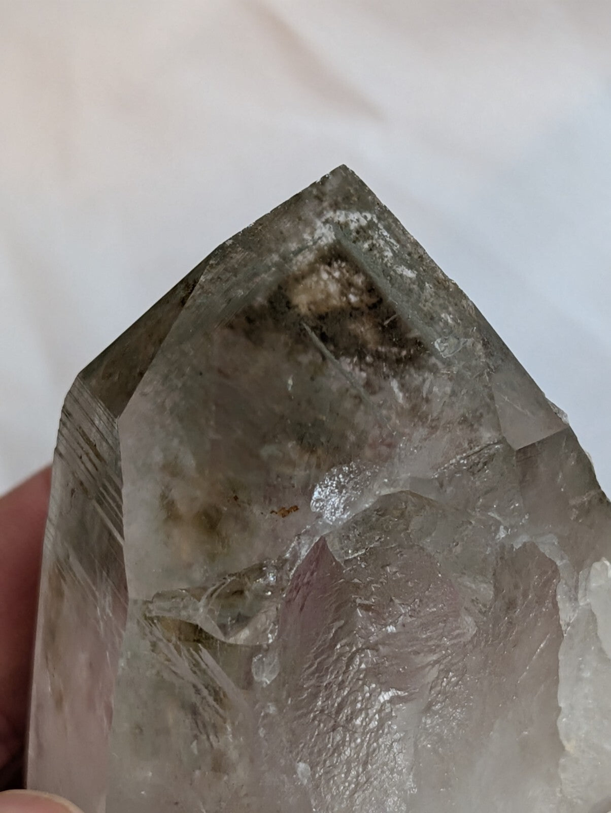 A translucent, grayish-white quartz crystal with natural inclusions and a pointed, faceted top.