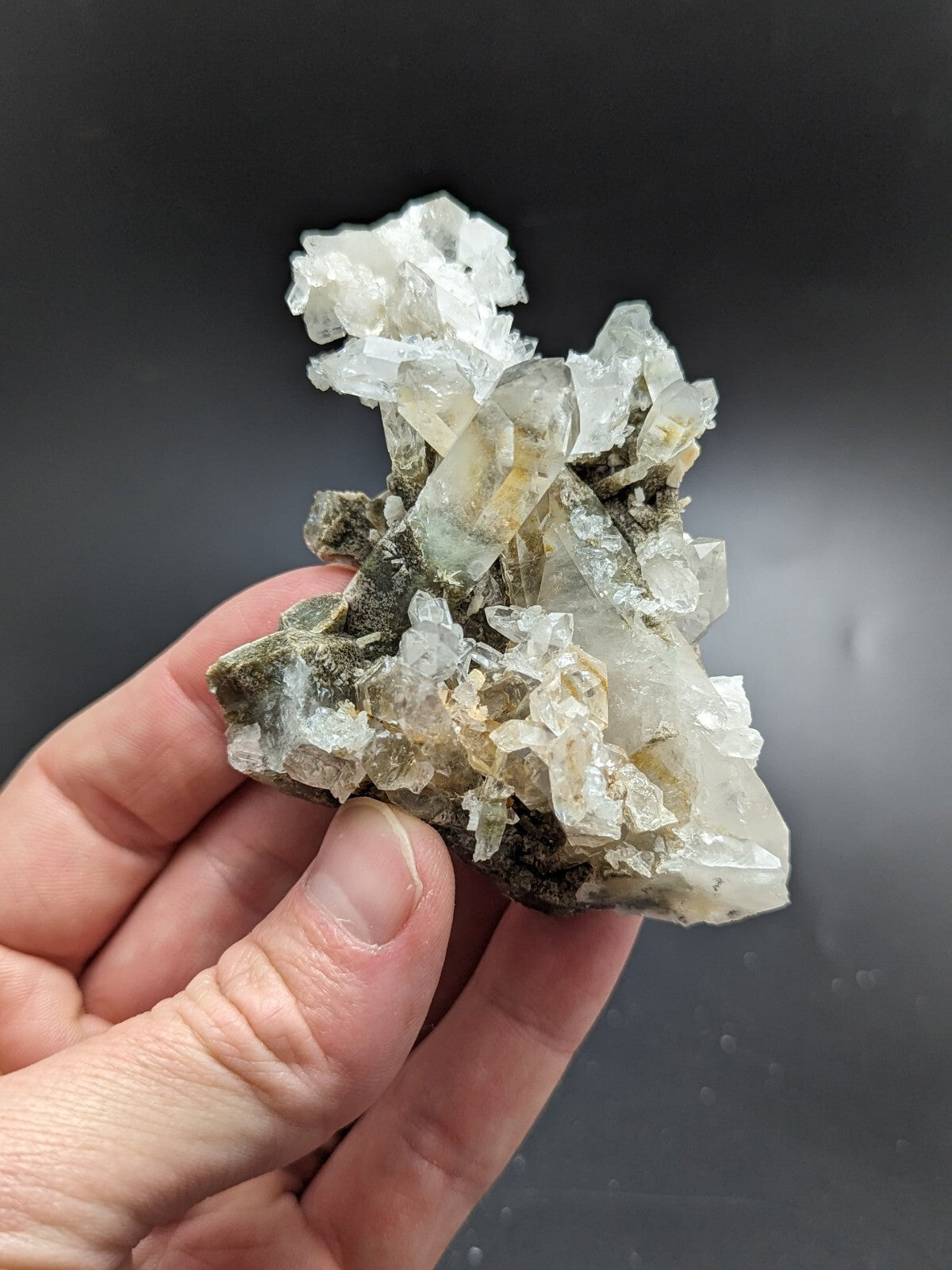 A translucent, crystalline mineral specimen with clear and pale yellowish quartz crystals growing from a dark green matrix.