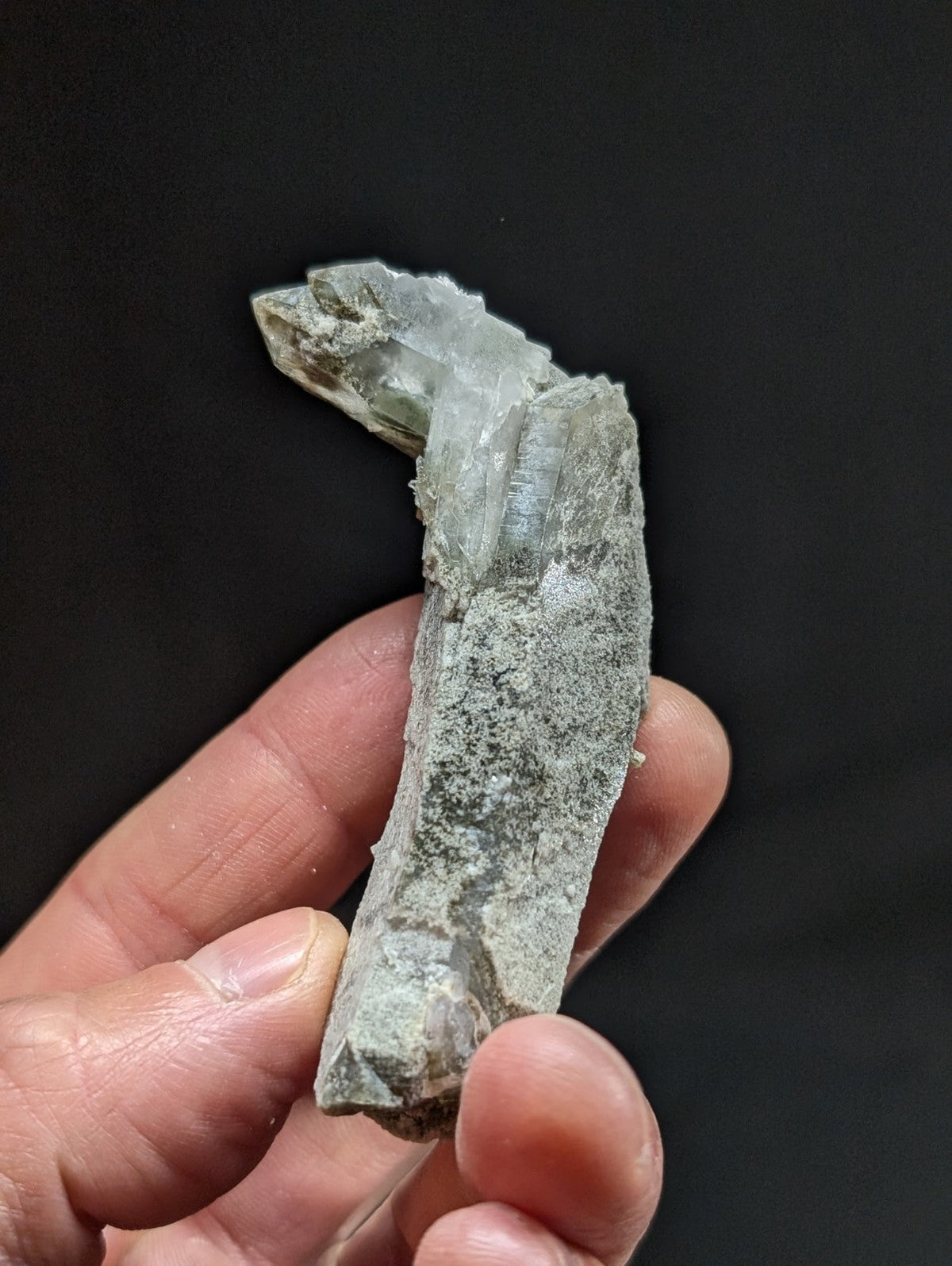 A translucent, pale green crystal formation with a jagged top and rough, earthy base.