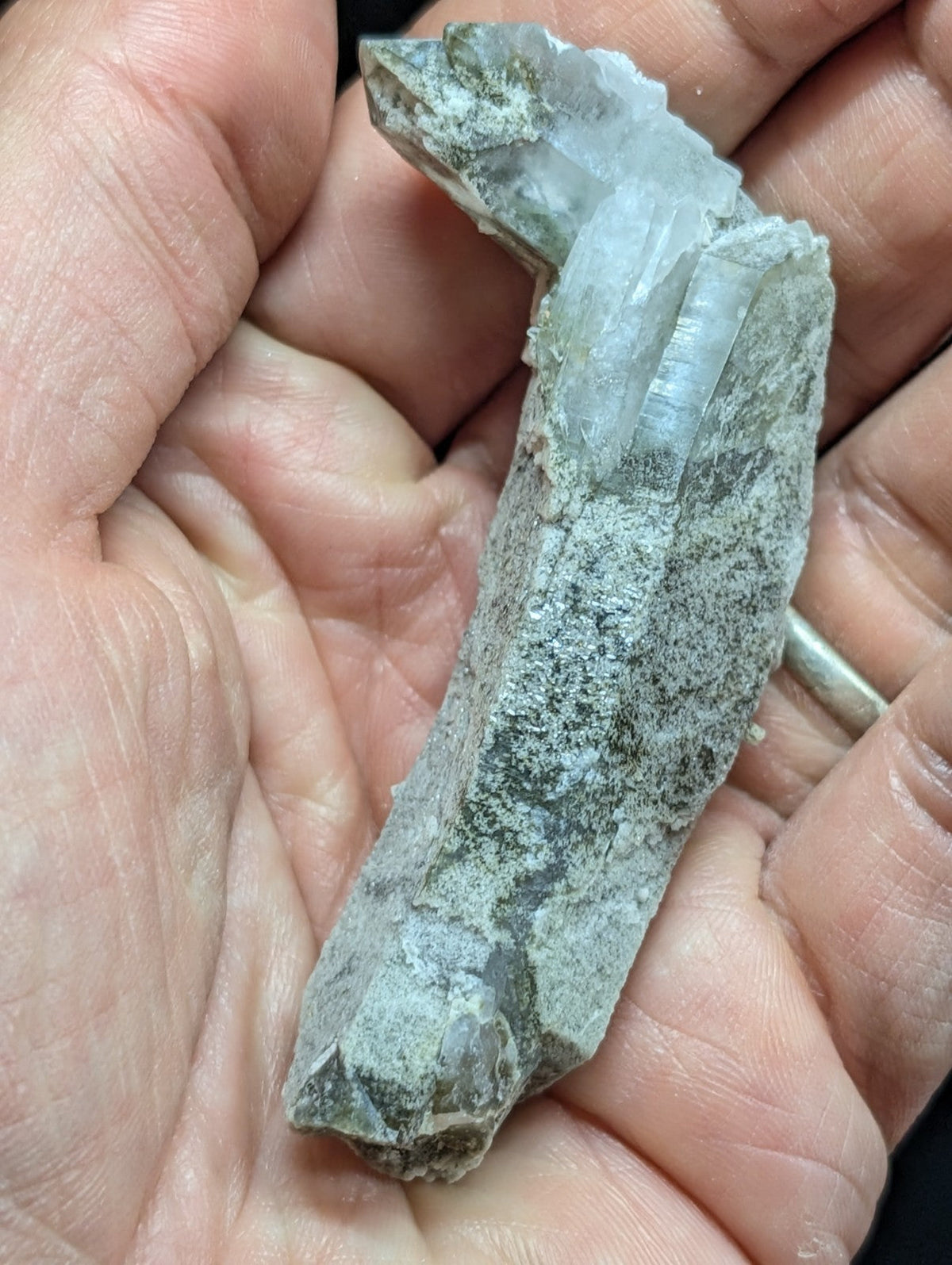 A translucent, pale gray quartz crystal cluster emerging from a rougher, darker matrix rock.