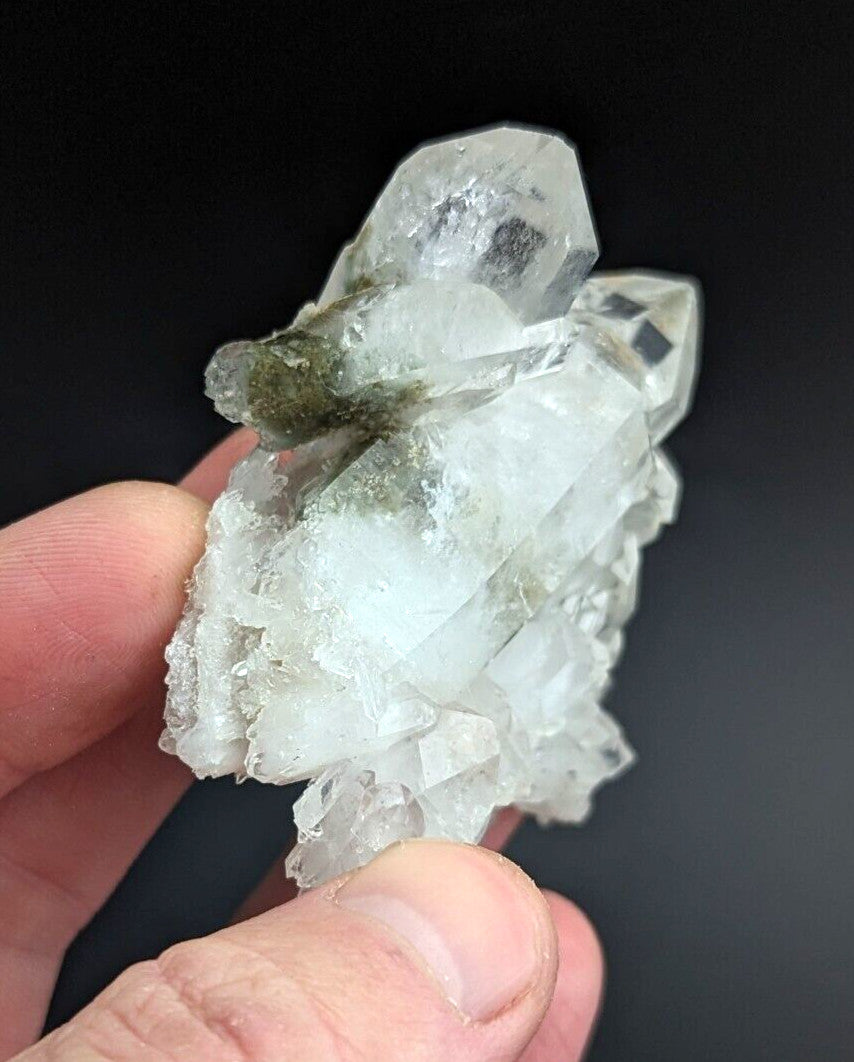 A translucent quartz crystal cluster with clear, faceted points and a patch of greenish mossy growth on its surface.