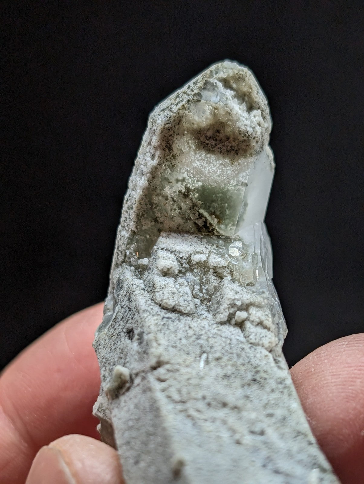 A translucent green crystal embedded in a gray, mineral-rich matrix.