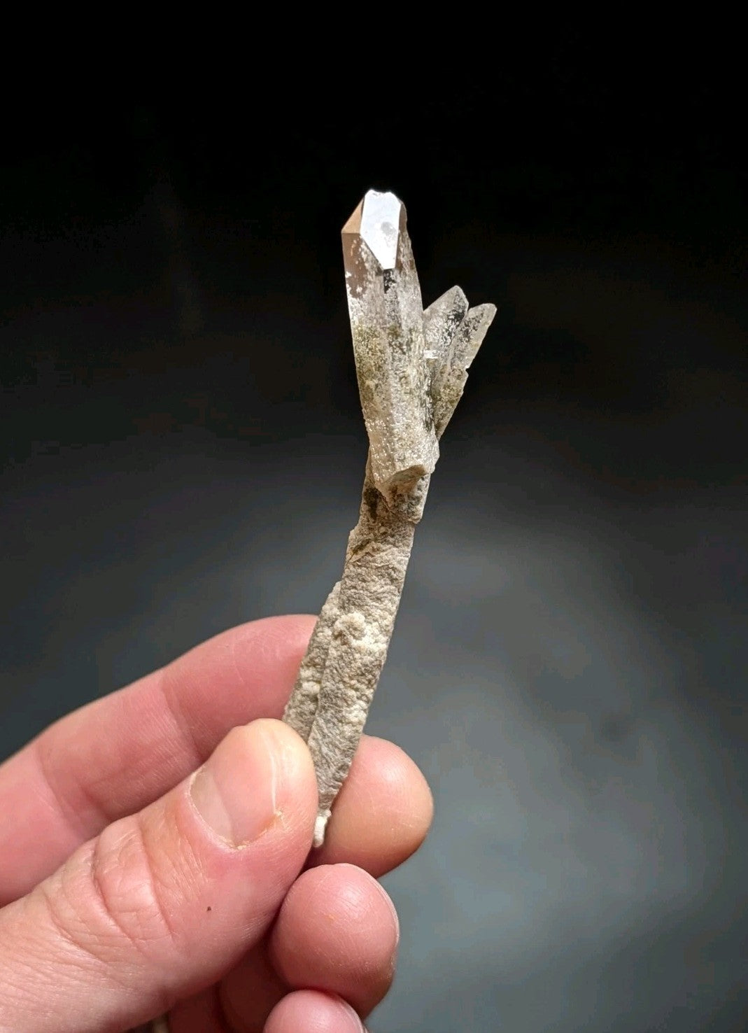 A translucent, pale quartz crystal cluster with a rough, earthy base and sharp, faceted points.