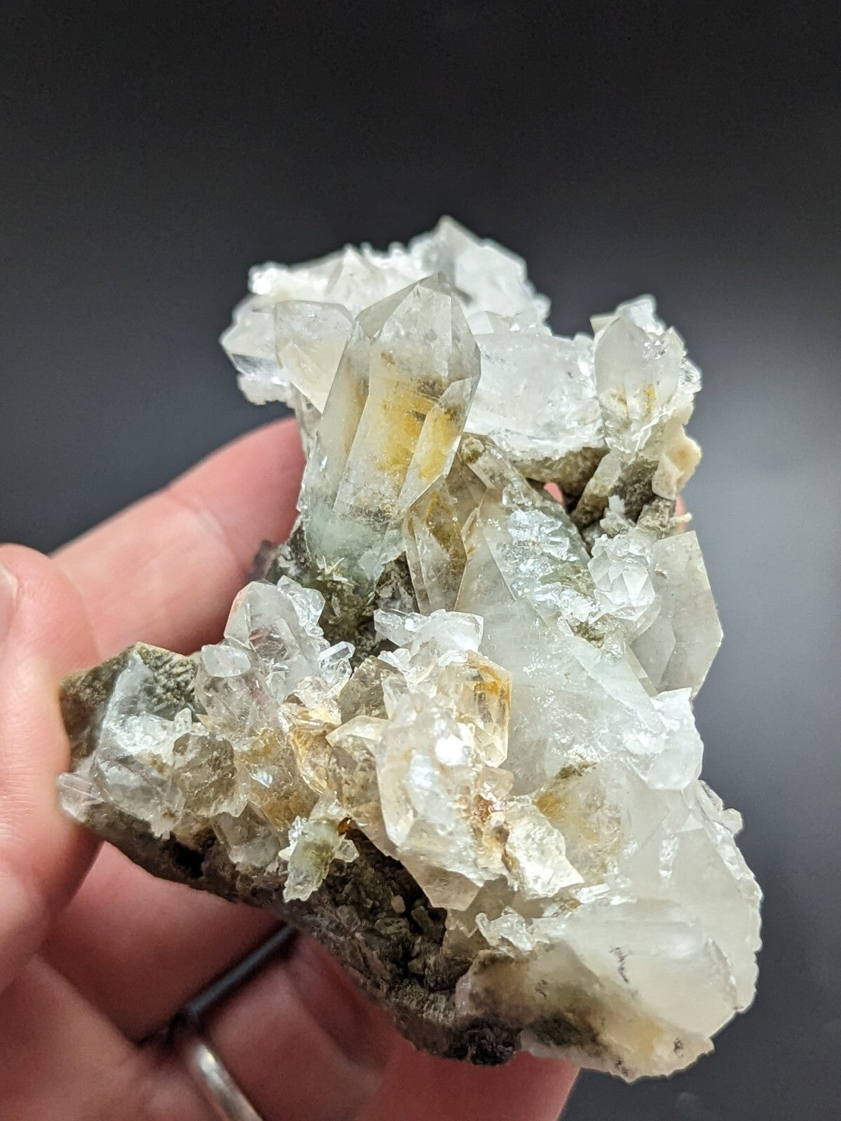 A translucent quartz crystal cluster with clear, faceted points and subtle yellowish inclusions set against a dark background.