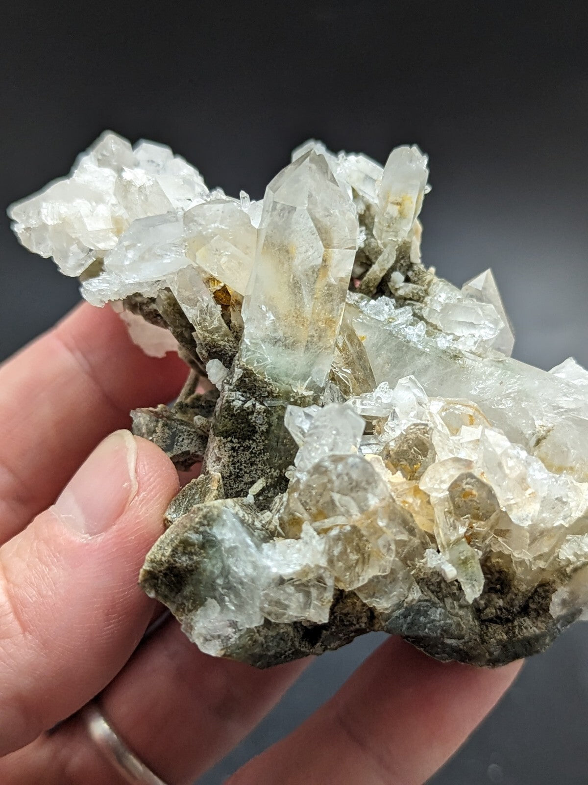 A translucent quartz crystal cluster with clear, pointed formations and subtle yellowish hues set against a dark matrix.