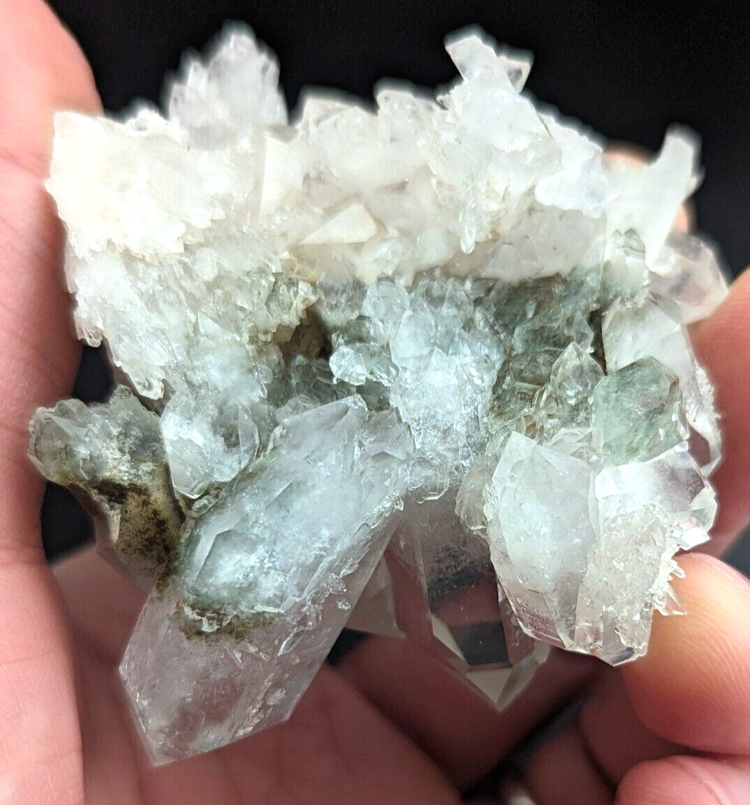 A cluster of translucent, pale green and clear quartz crystals with jagged edges held in a hand.