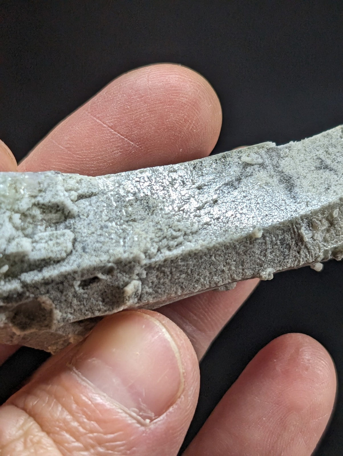 A weathered, gray concrete fragment with a rough, textured surface and visible embedded particles.