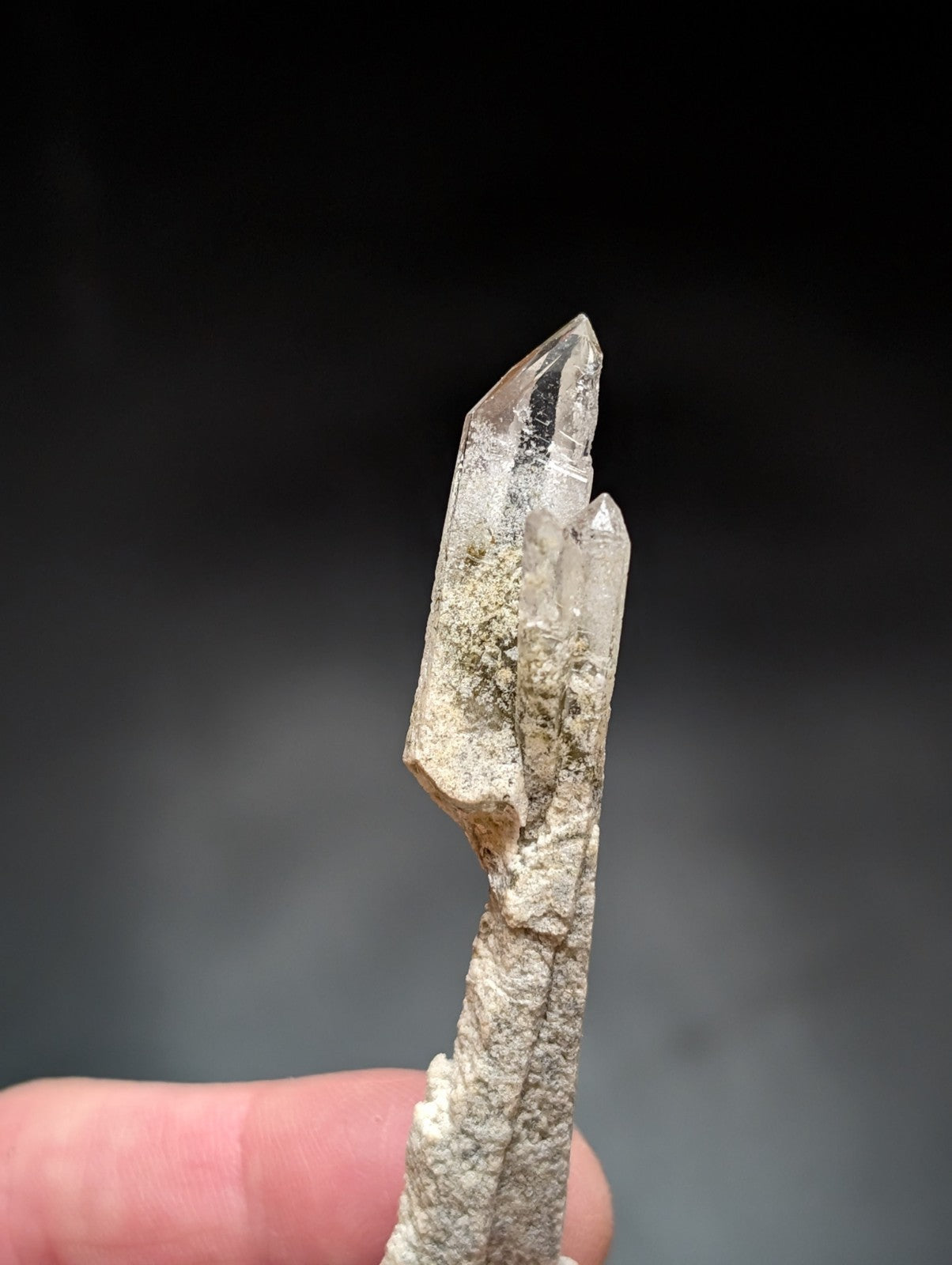 A translucent, clear quartz crystal with a pointed tip and visible internal inclusions, mounted on a rough-textured base.