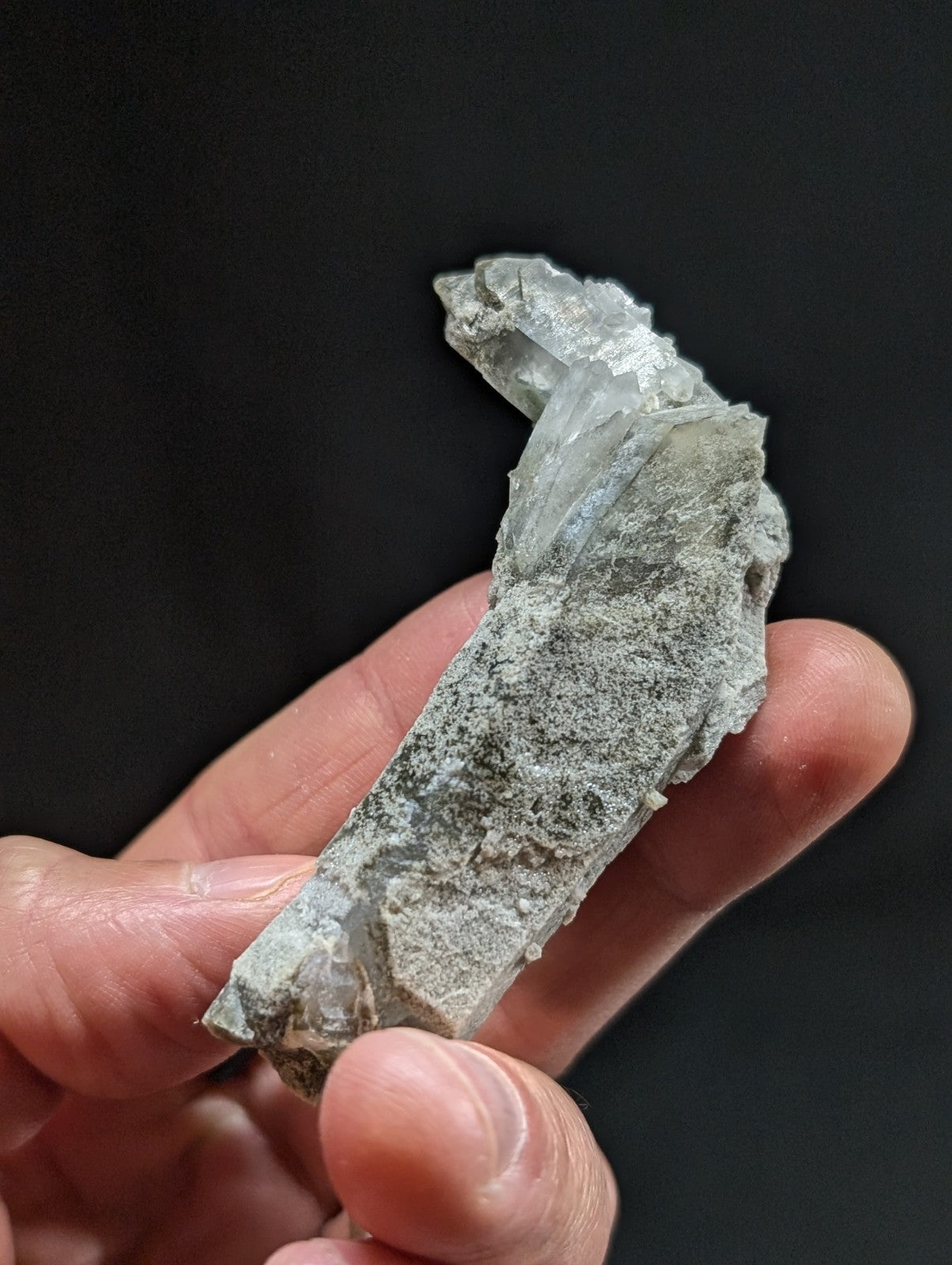 A translucent, pale gray crystal cluster with jagged edges and a rough, mineral-rich base.