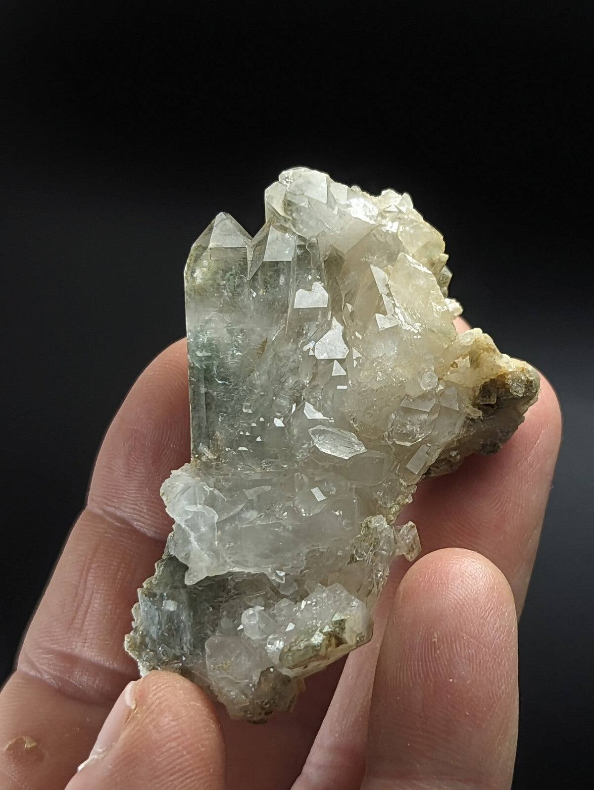 A translucent green and white quartz crystal cluster with sharp, faceted points held in a hand.