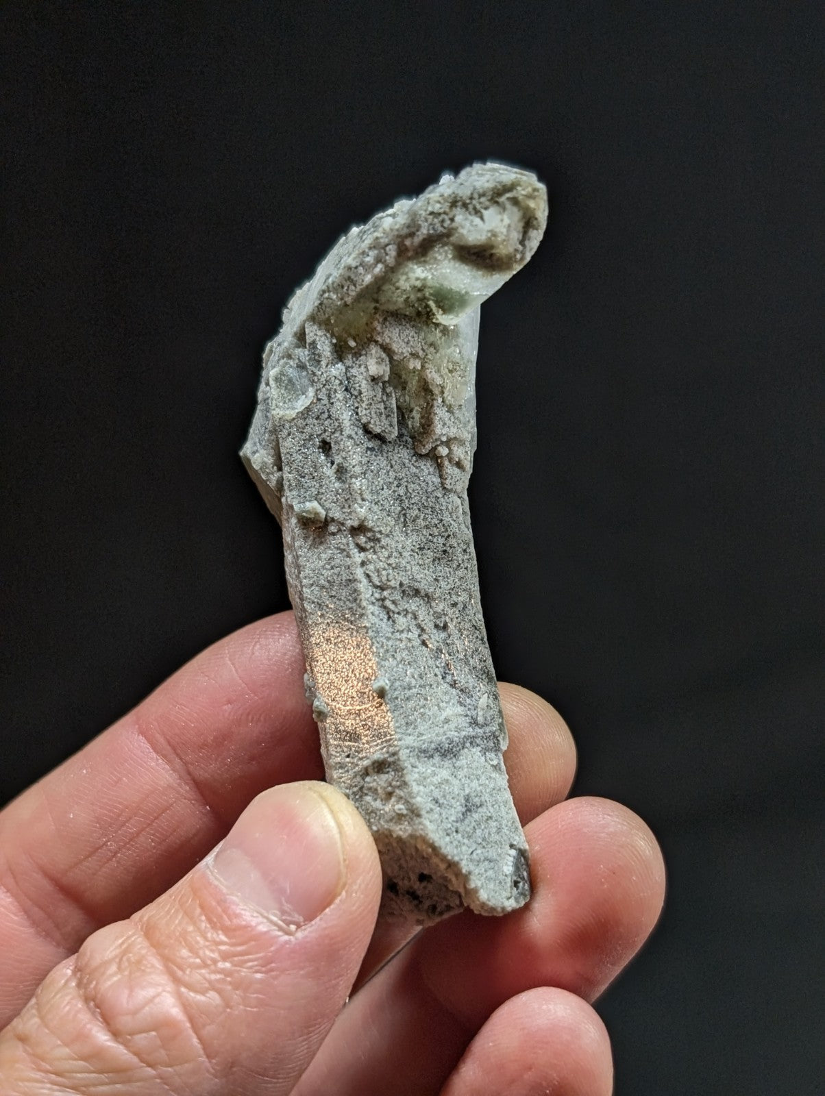 A weathered, gray-green jade fragment with a rough, textured surface and visible natural imperfections.