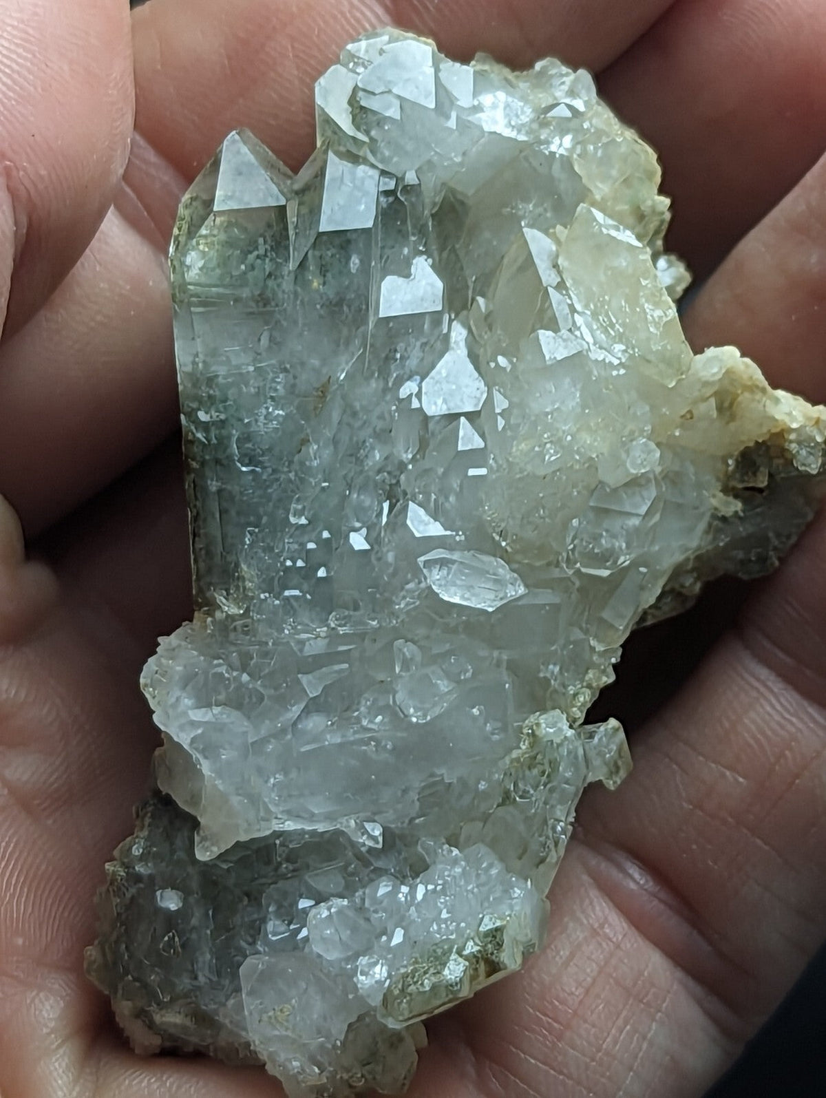 A translucent, pale greenish-white quartz crystal cluster with sharp, faceted points and a rough, earthy base.