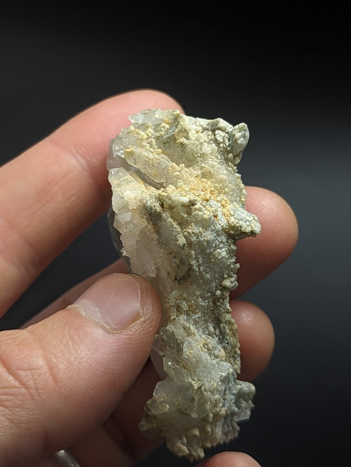 A translucent, pale greenish-white mineral specimen with a rough, crystalline texture and patches of yellowish matrix.