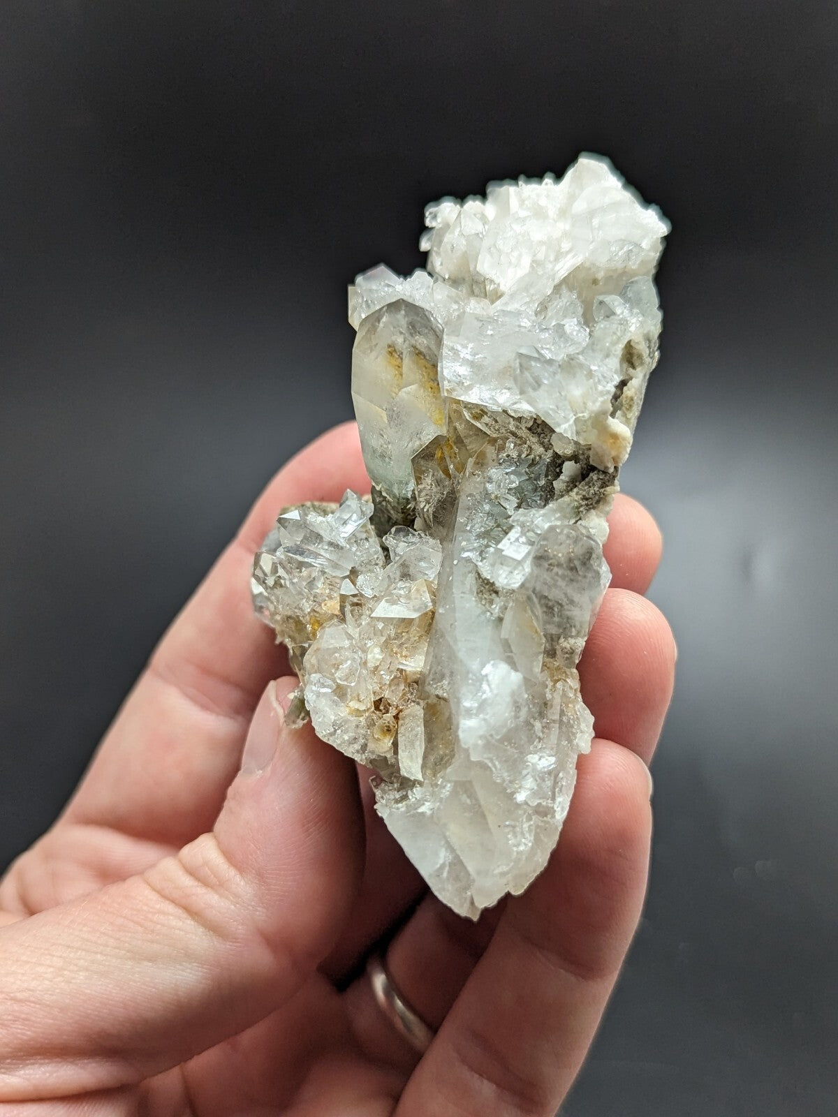 A hand holds a translucent white quartz crystal cluster with clear, faceted formations and subtle yellowish inclusions.