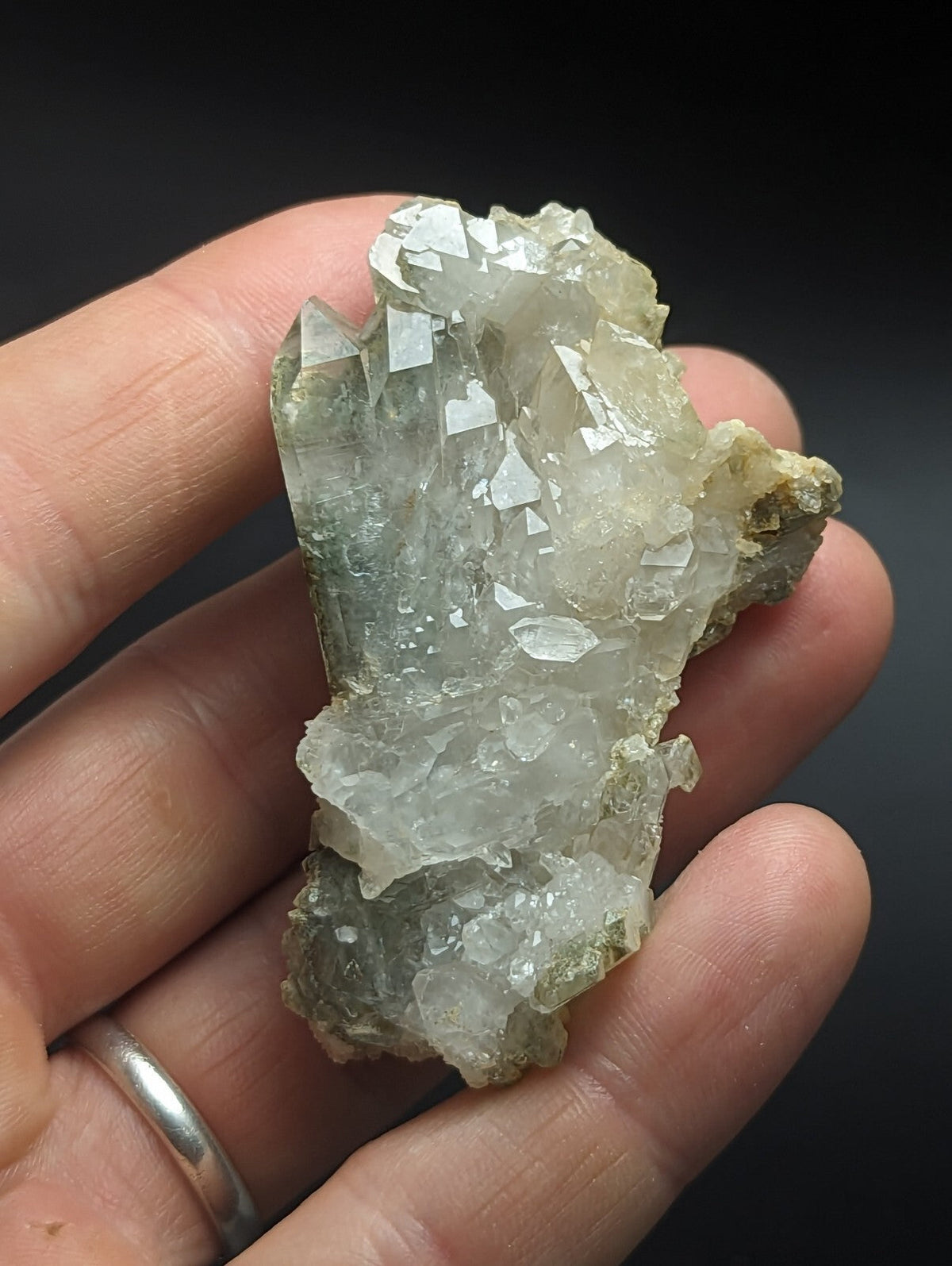 A translucent, pale greenish-white quartz crystal cluster with sharp, faceted points and a rough, earthy base.