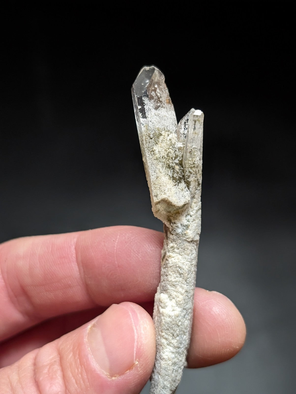 A translucent quartz crystal cluster with a rough, grayish matrix base and two prominent clear prismatic points.