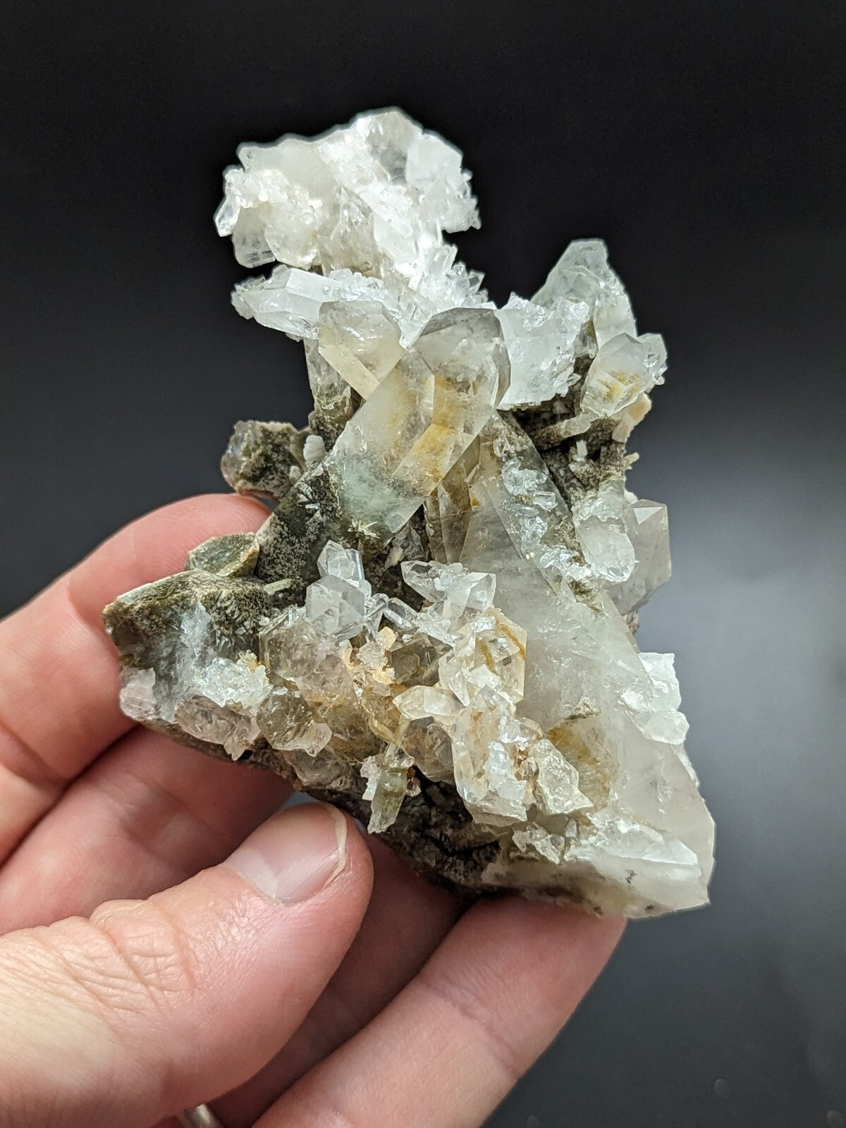 A translucent quartz crystal cluster with clear, faceted points and subtle yellowish-green hues nestled in a dark green matrix.