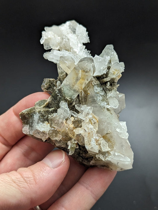 A translucent quartz crystal cluster with clear, faceted points and subtle yellowish-green hues nestled in a dark green matrix.