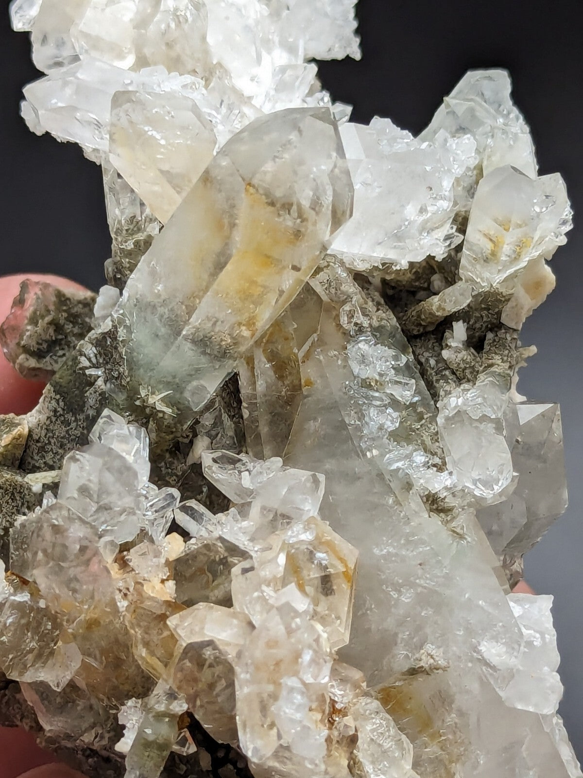 A cluster of translucent quartz crystals with subtle yellow and green inclusions, set against a dark background.