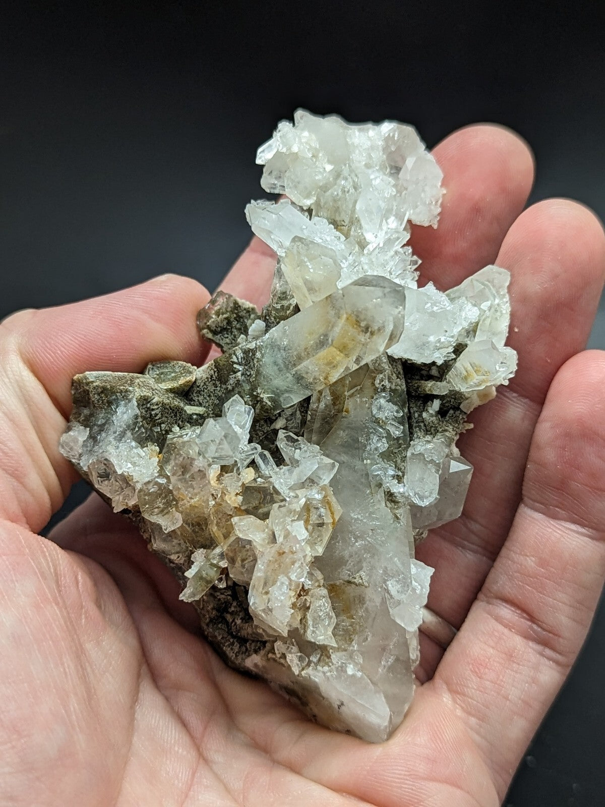 A translucent, crystalline quartz cluster with clear and slightly yellowish facets nestled in a dark matrix.