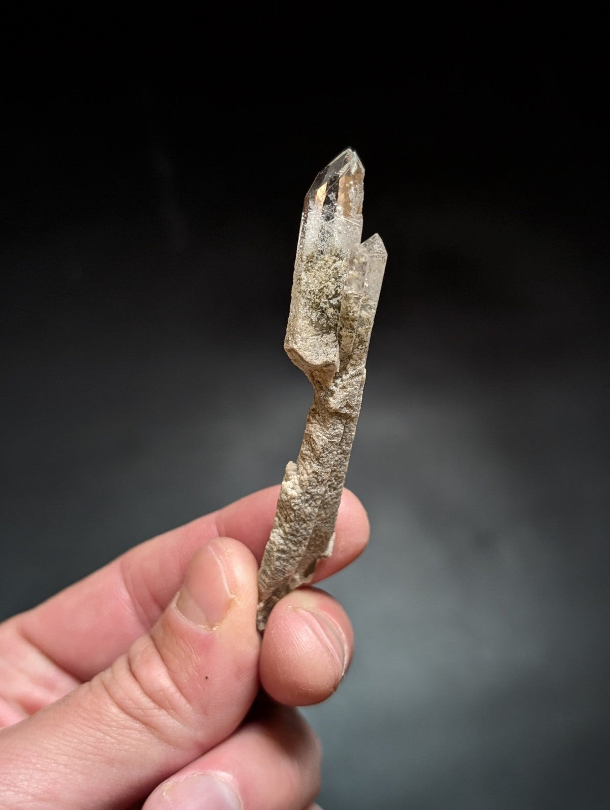A translucent, pointed quartz crystal with a rough, earthy base and clear facets at the top.