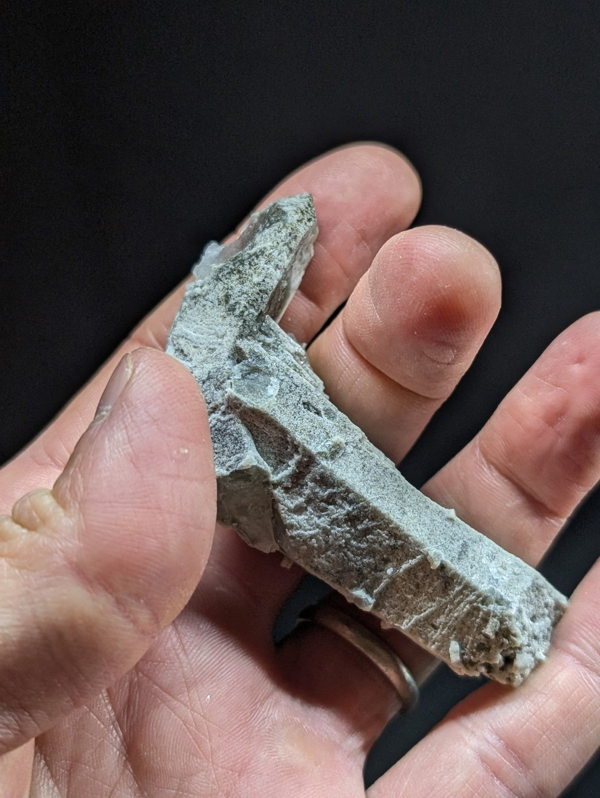 A rough, grayish-green stone fragment with a jagged edge and uneven surface.
