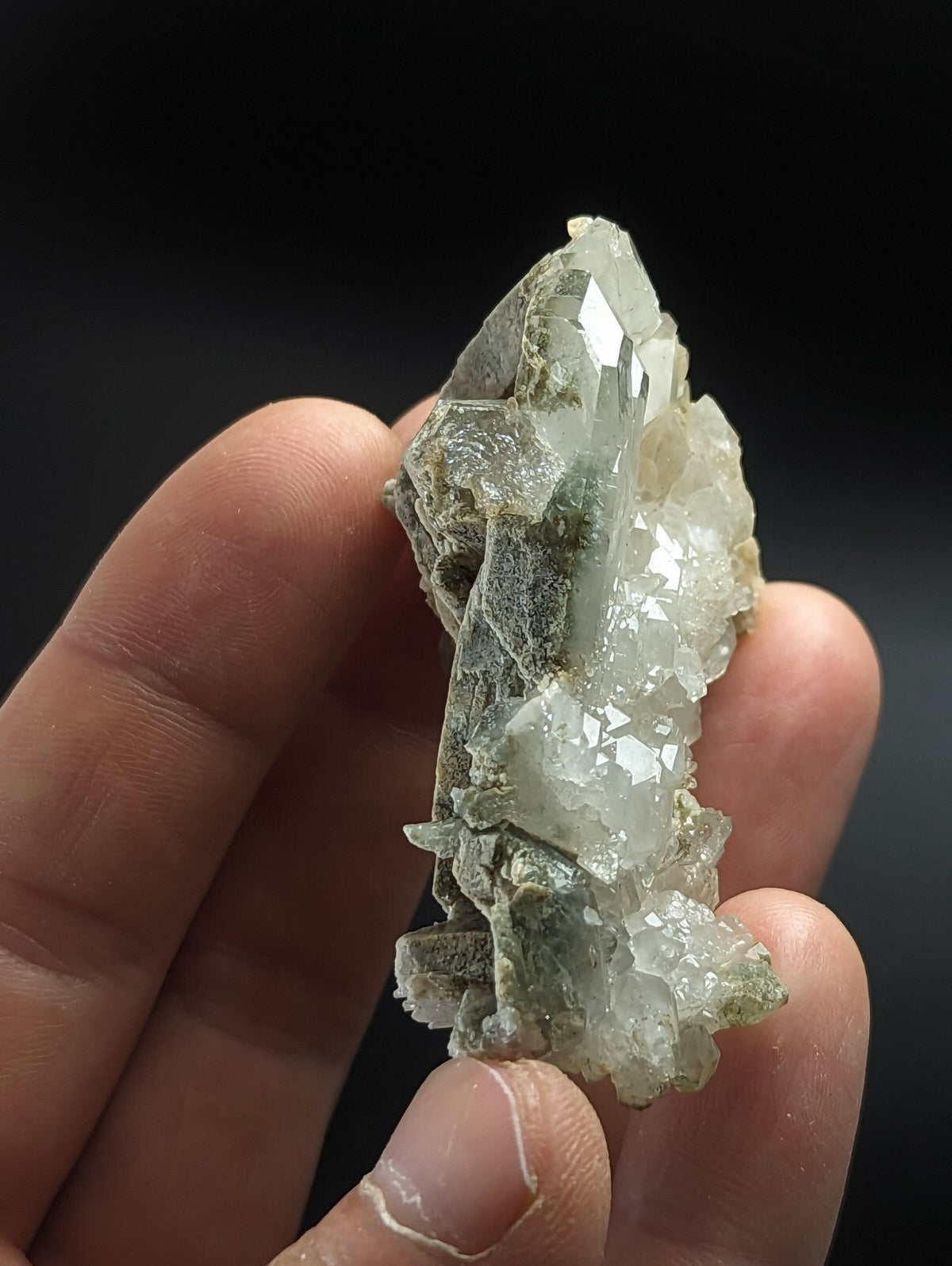 A translucent green and white mineral crystal cluster with sharp, faceted points held in a hand.