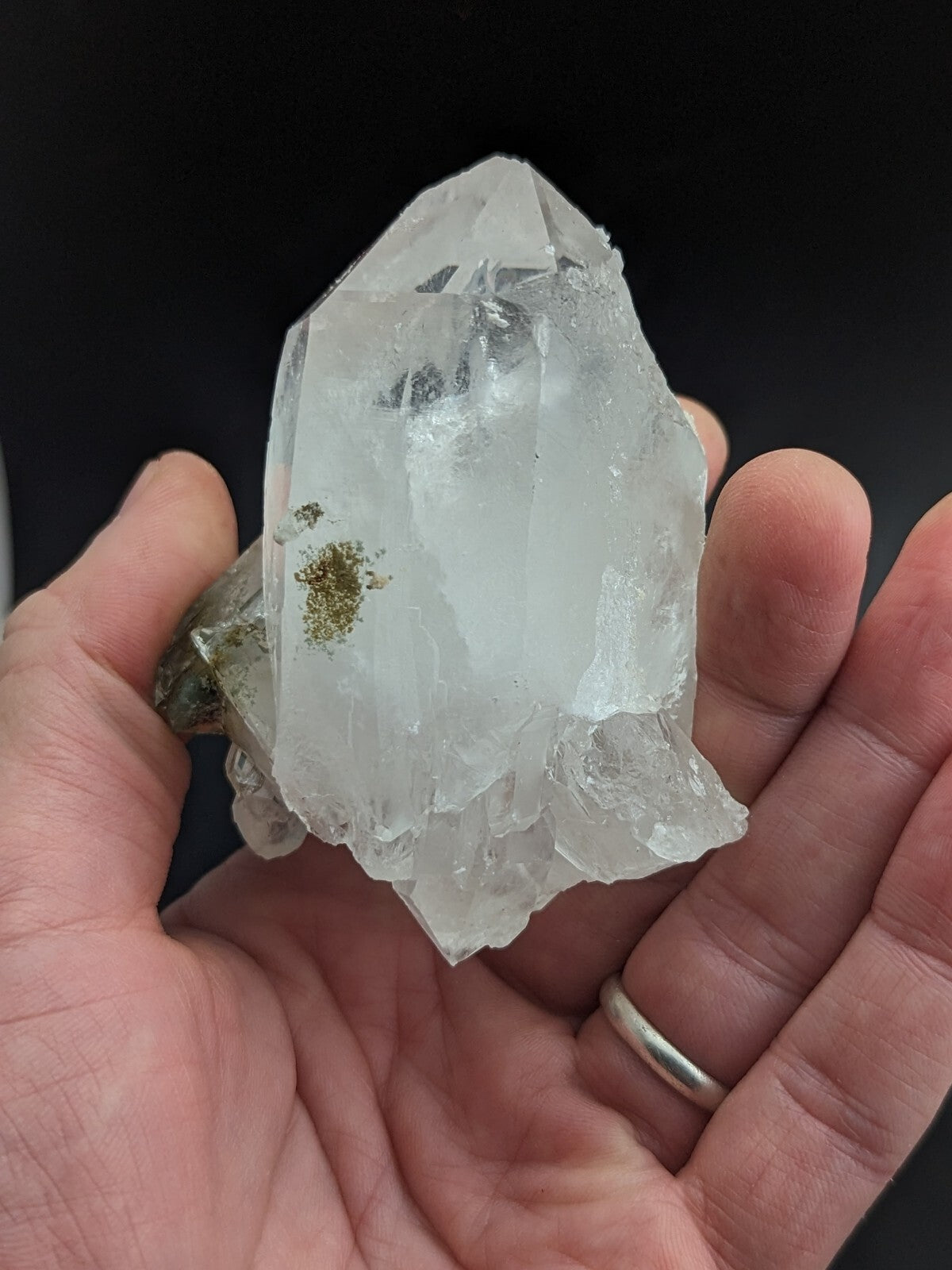 A translucent white quartz crystal with a pointed tip and natural facets, held in someone’s hand.