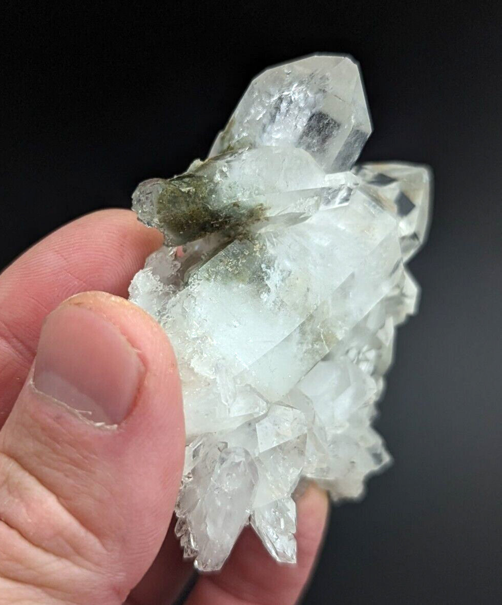 A translucent white quartz crystal cluster with sharp, faceted points and a small patch of greenish mossy growth on its surface.