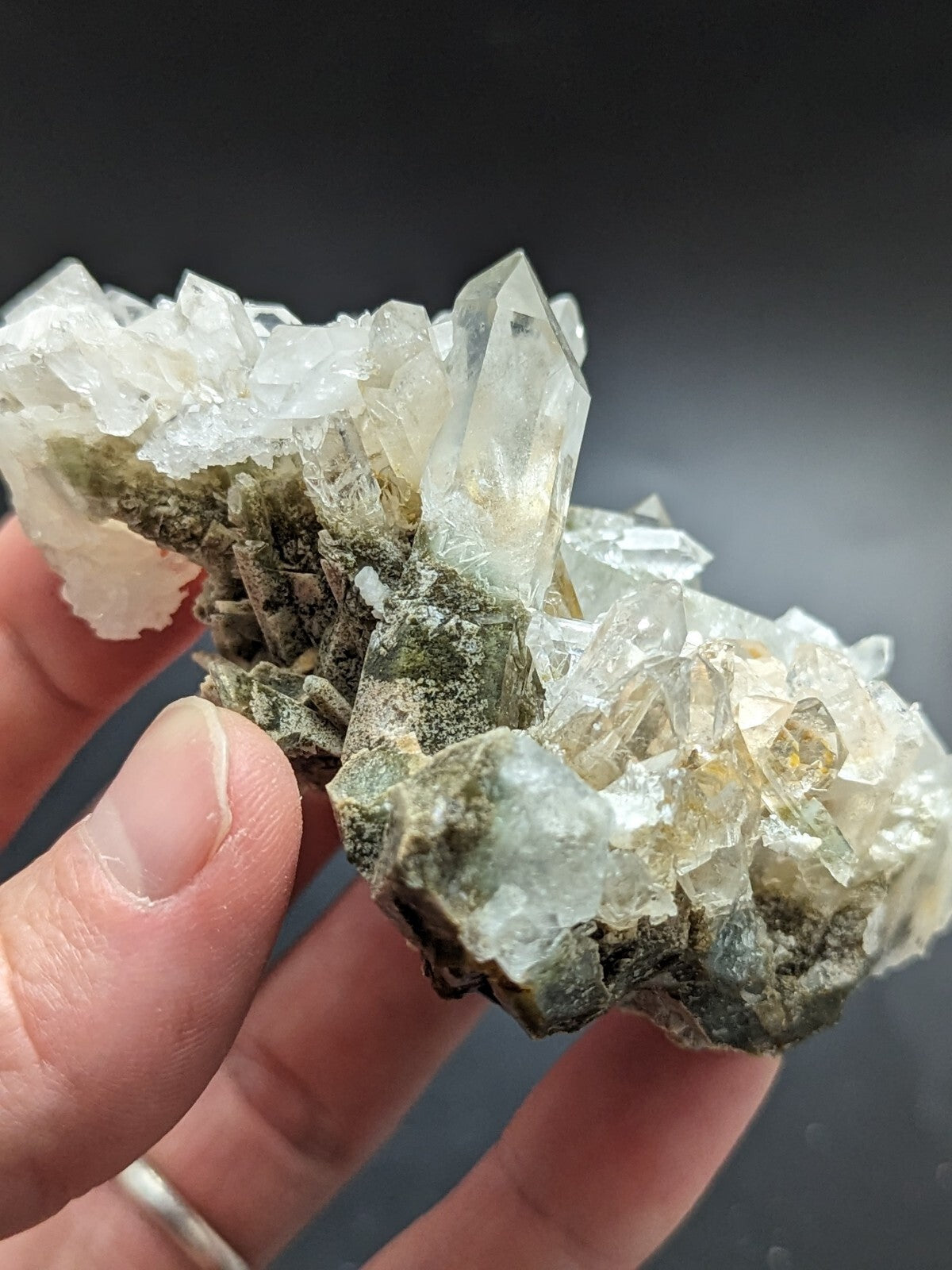 A cluster of translucent quartz crystals with clear, sharp facets and a greenish matrix base.