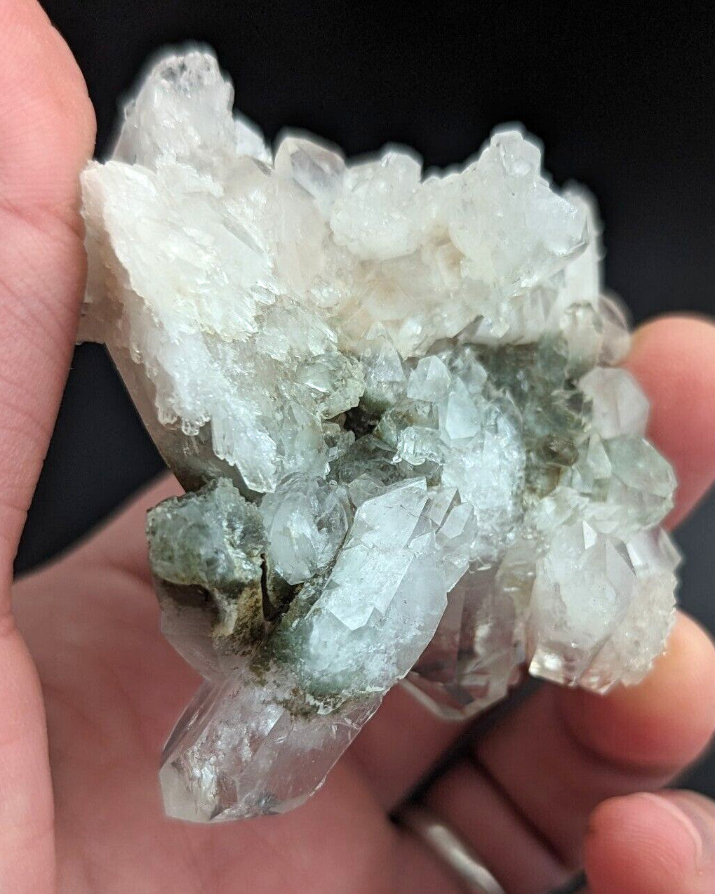 A cluster of translucent quartz crystals with a mix of clear and pale green hues, held gently in someone’s hand.